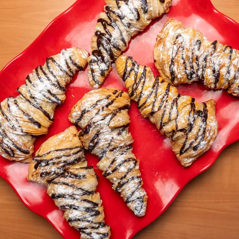 Several sfogliatelle pastries with chocolate drizzle and powdered sugar on a red platter.