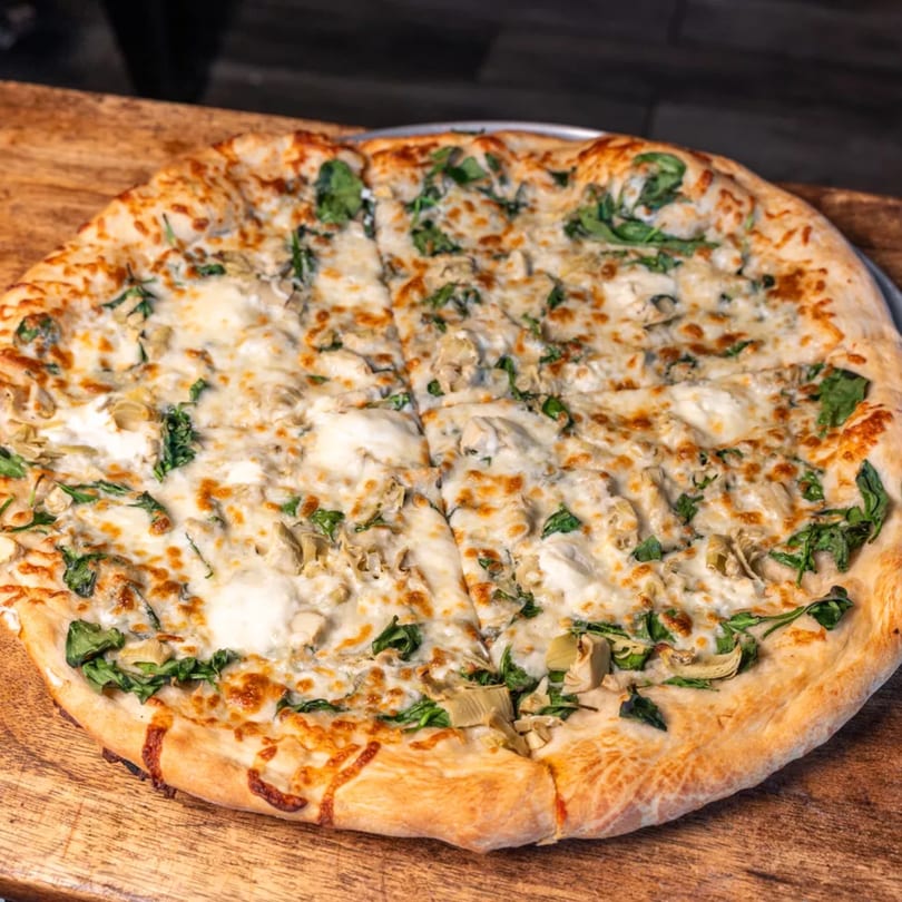 Capones Italian Eatery West's white pizza with spinach and artichoke hearts on a wooden board.